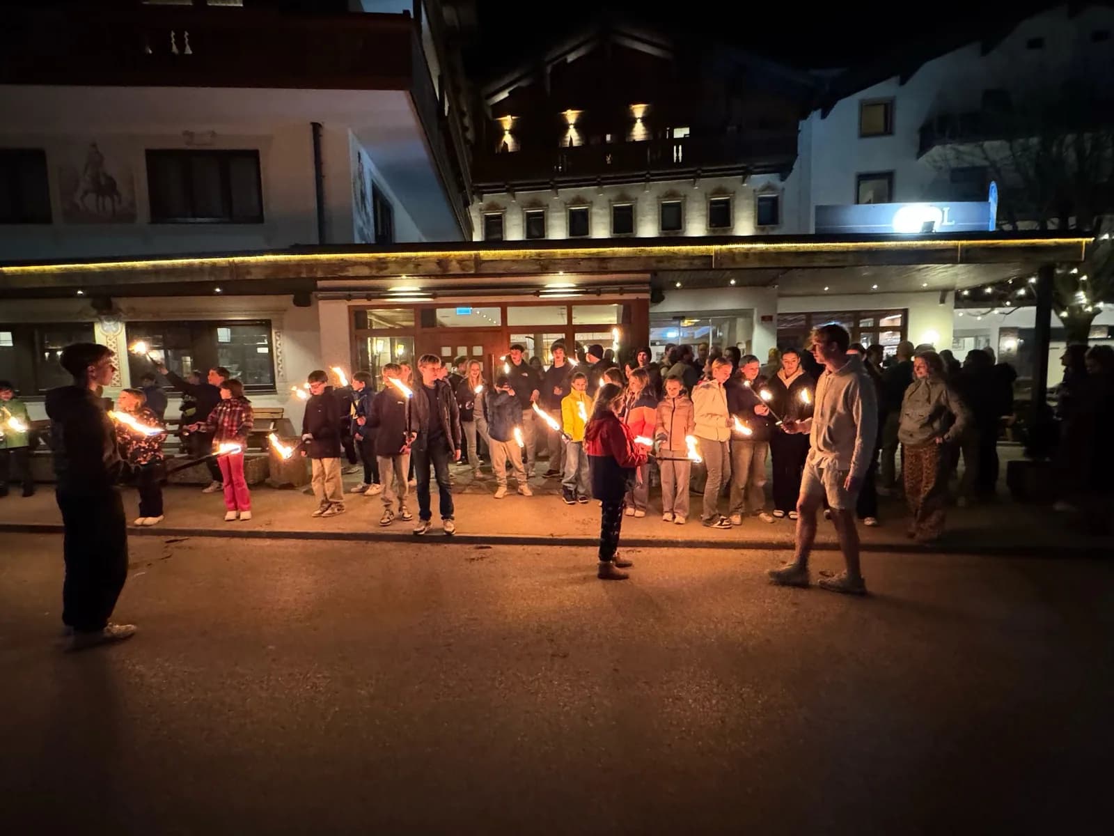De groep loopt in het donker met fakkels door het dorp, voor het hotel