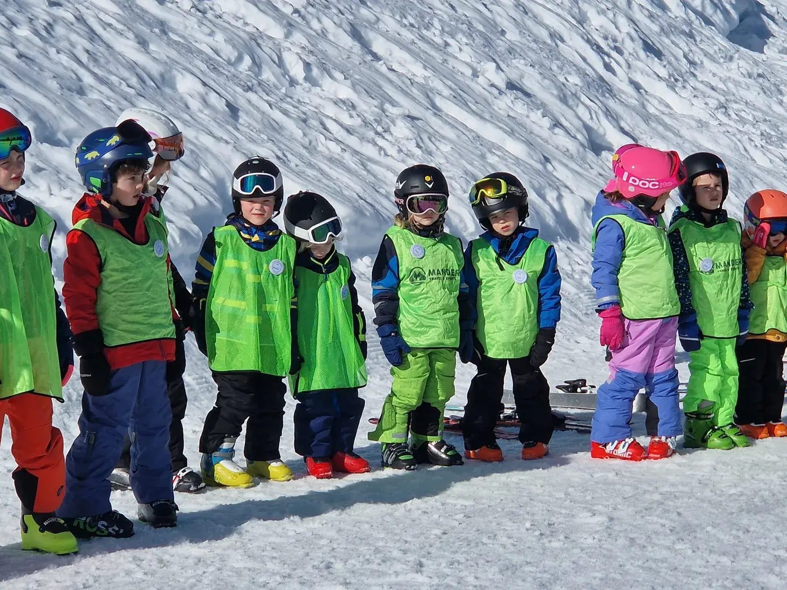 Een rij jonge kinderen in groene skihesjes staat klaar voor de les